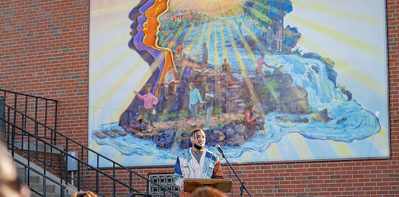Man stands at podium in front of a vibrant mural.